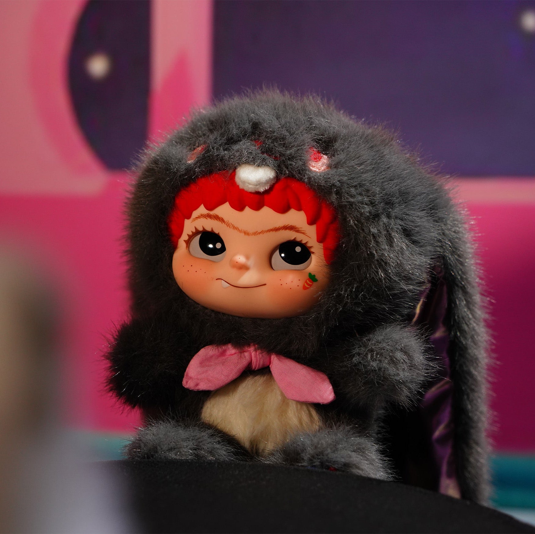 Toy figure with red hair and a pink bow in a colorful setting